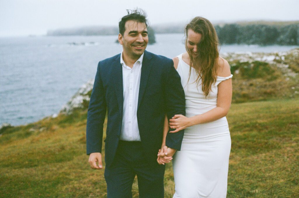 bride and groom hold hands on a sea cliff with sea stacks in background during Bonavista elopement