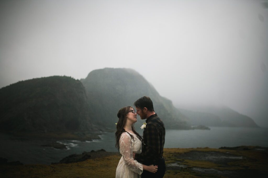 bride and groom kiss on a rainy hiking trail with mountains in the background during Newfoundland elopement