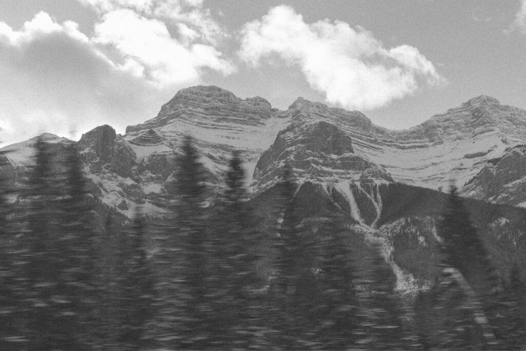 black and white photo of mountains in Banff National Park with a foreground of trees blurred by motion