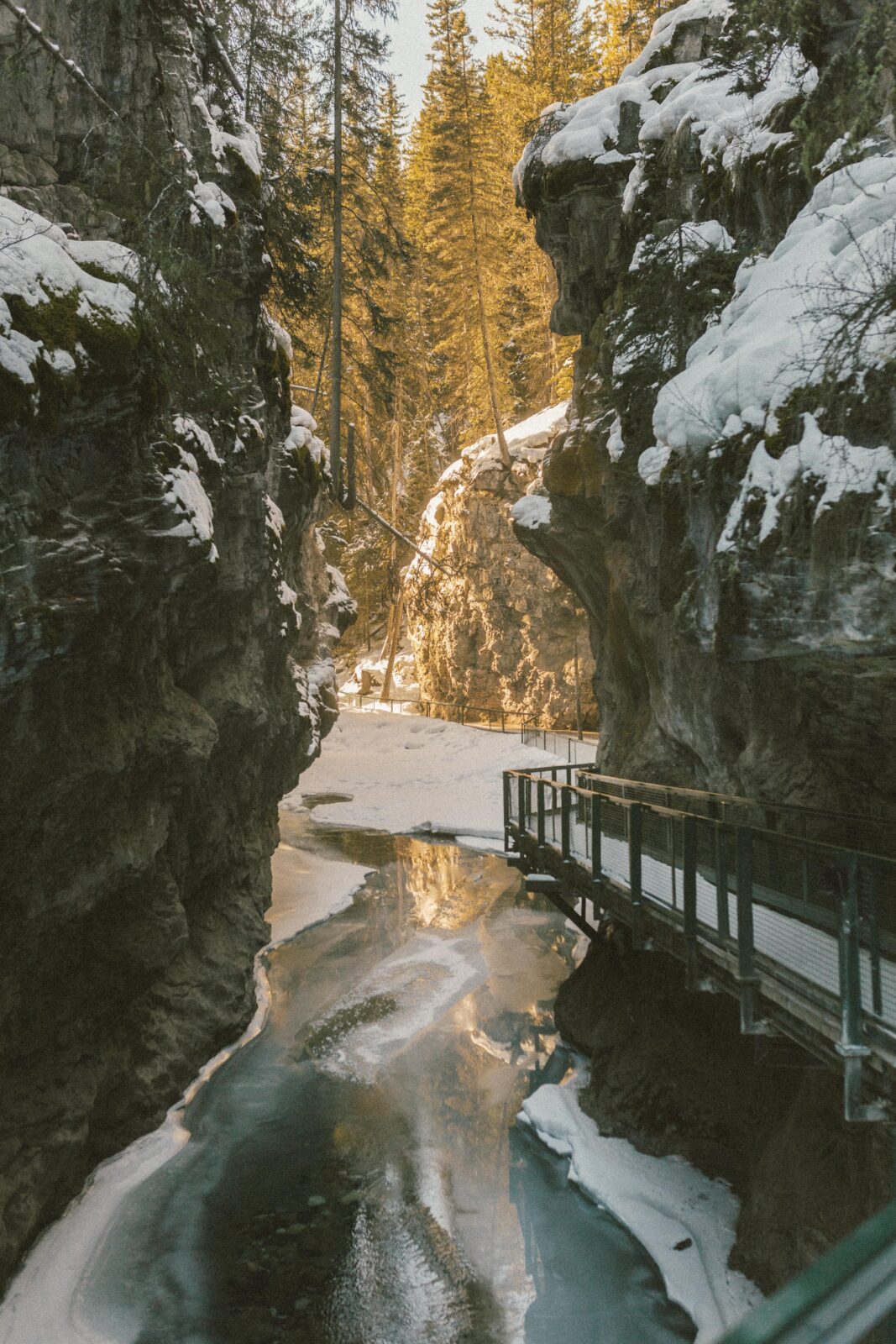 The golden winter sun illuminates an icy Johnston Canyon in Banff National Park