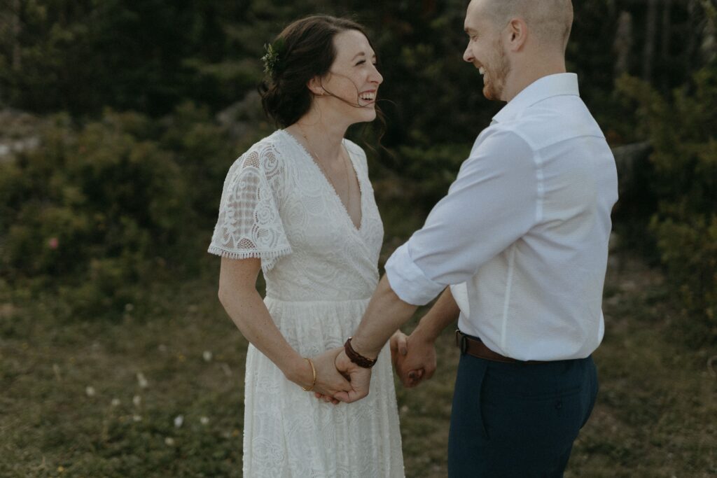 bride and groom hold hands and laugh with greenery in the background