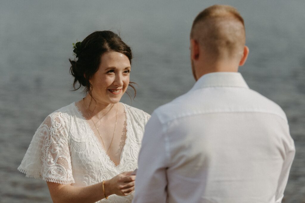 bride grins as she reads vows during elopement ceremony on the lake shore
