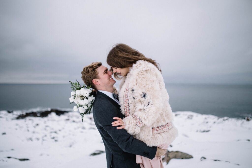 bride and groom laugh in a snowy landscape as groom picks the bride up