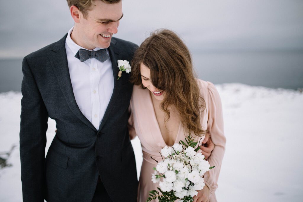 Bride and groom laugh and walk through snowy landscape on Fogo Island