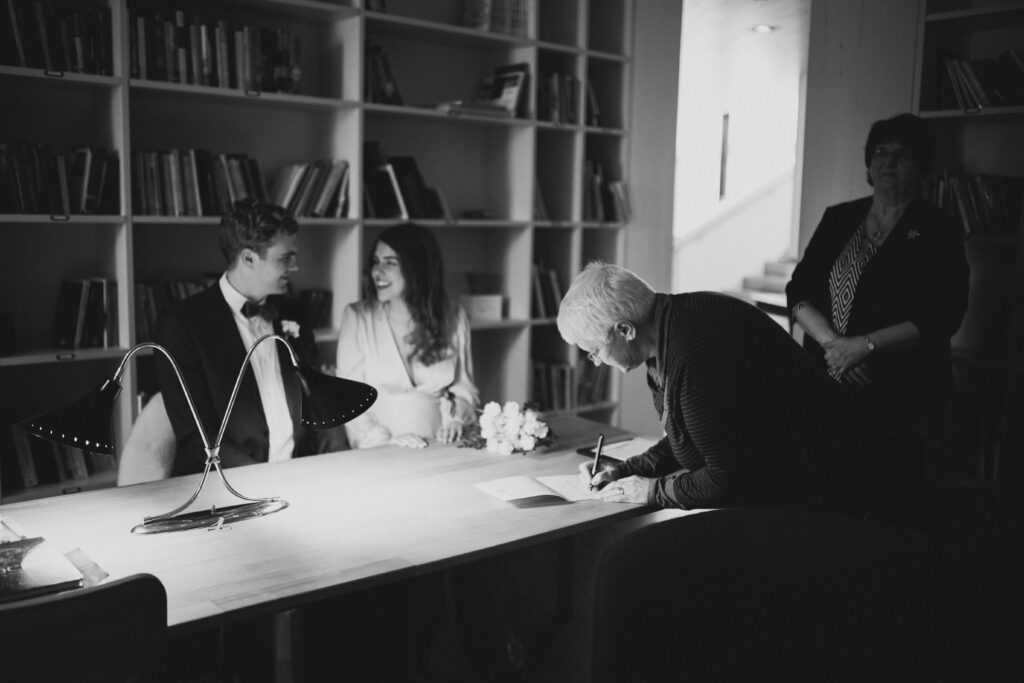 bride and groom grin at each other as witnesses sign their marriage license at the Fogo Island Inn