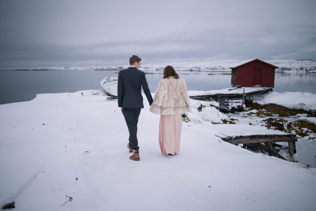 brdie and groom walk towards a red fishing stage in the snow on Fogo Island