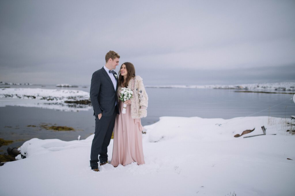 bride and groom smile at each other in a snowy barren landscape