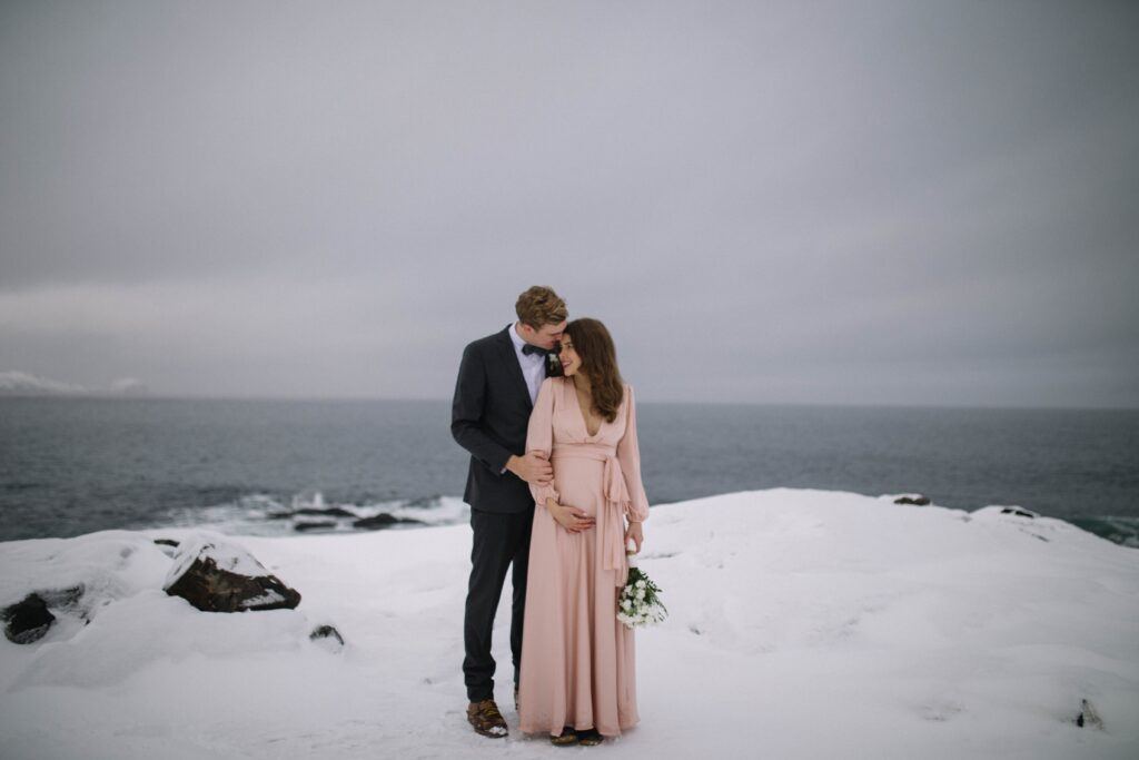 Bride and groom hold each other and their baby bump on a wintry Fogo Island.