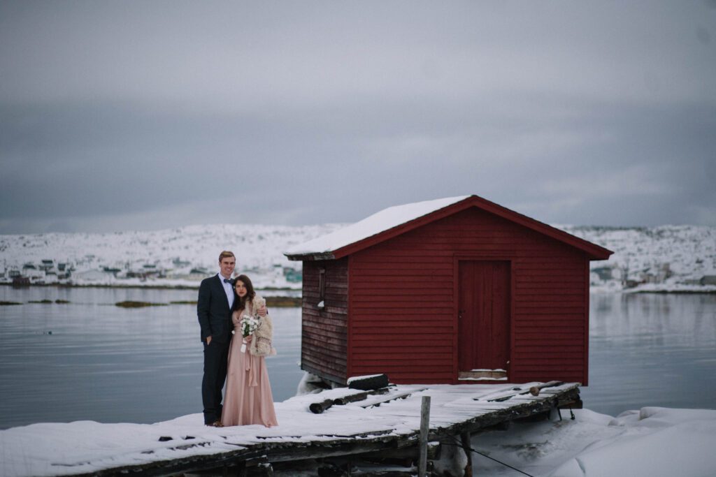 bride and groom hold each other beside a red fishing stage on Fogo Island