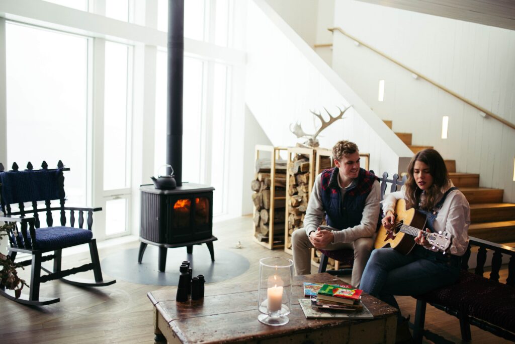 bride plays guitar for groom by the fire inside the Fogo Island Inn