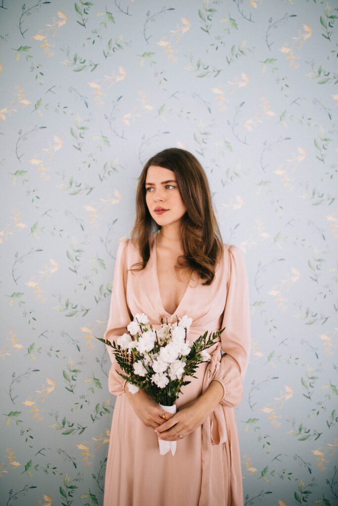 Bride holding bouquet beside blue floral wallpaper in the Fogo Island Inn