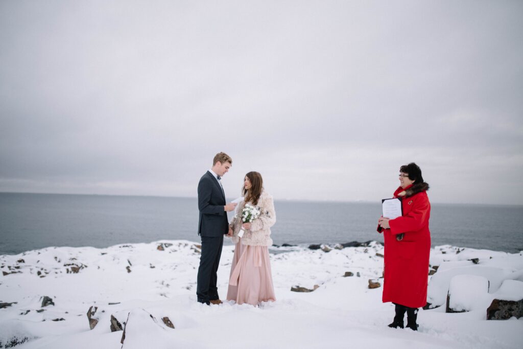 groom reads vows while holding bride's hand in a barren, snowy landscape