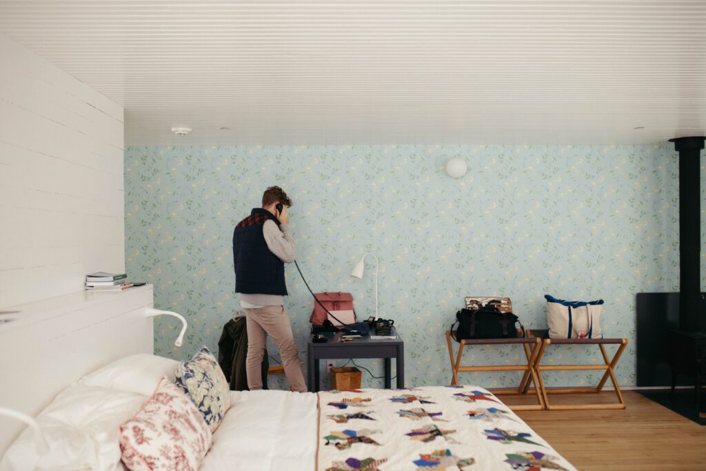 Groom makes a phone call in his room at the Fogo Island Inn, featuring blue floral wallpaper.