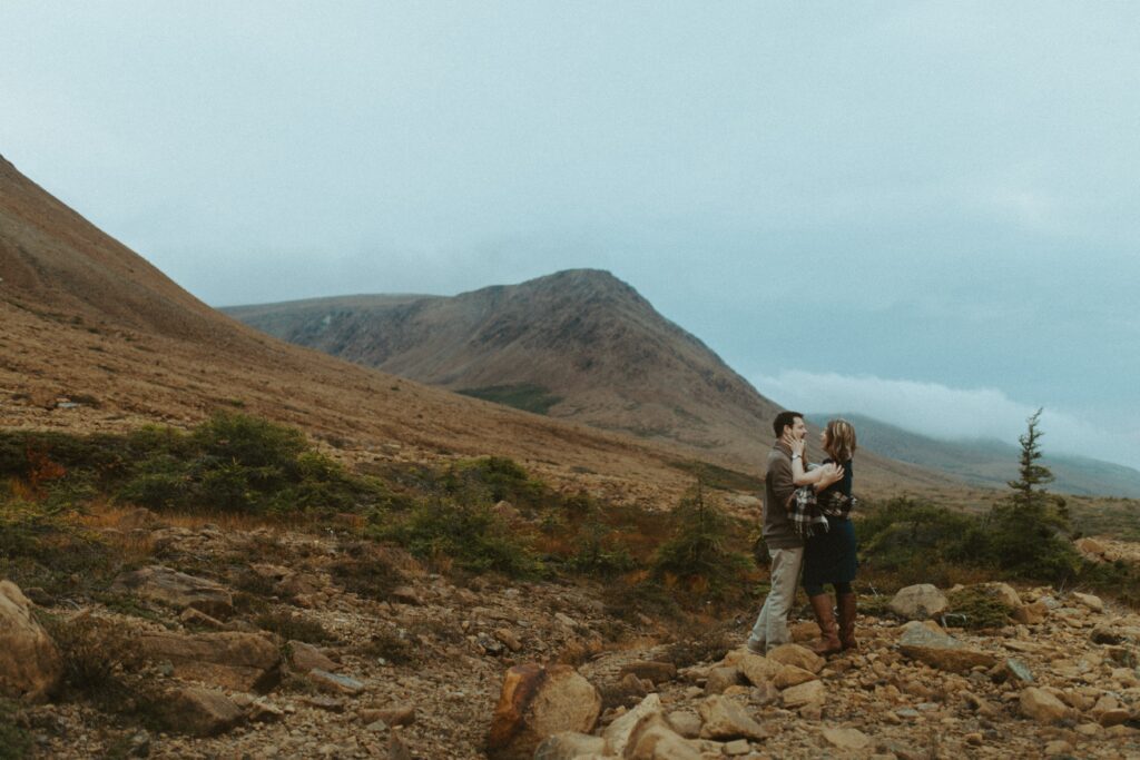 couple hold each other on the rust-red rocks of The Tablelands in Gros Morne National Park
