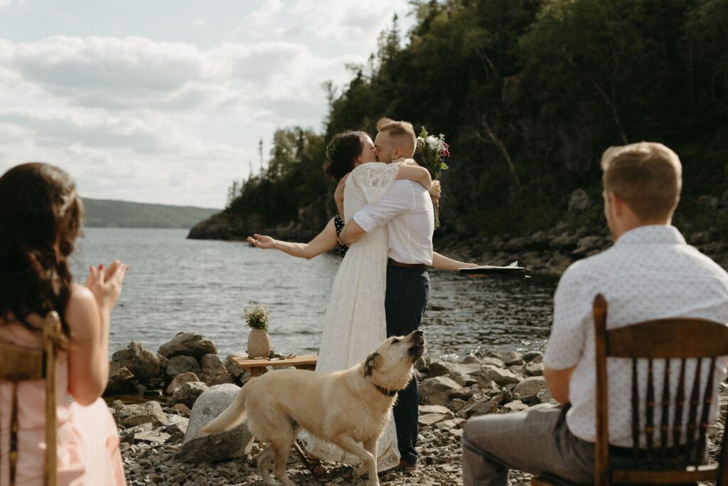 dog howls as bride and groom kiss during elopement ceremony on the beach