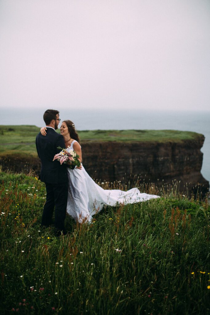 bride and room laugh on the edge of a sea cliff during Newfoundland elopement