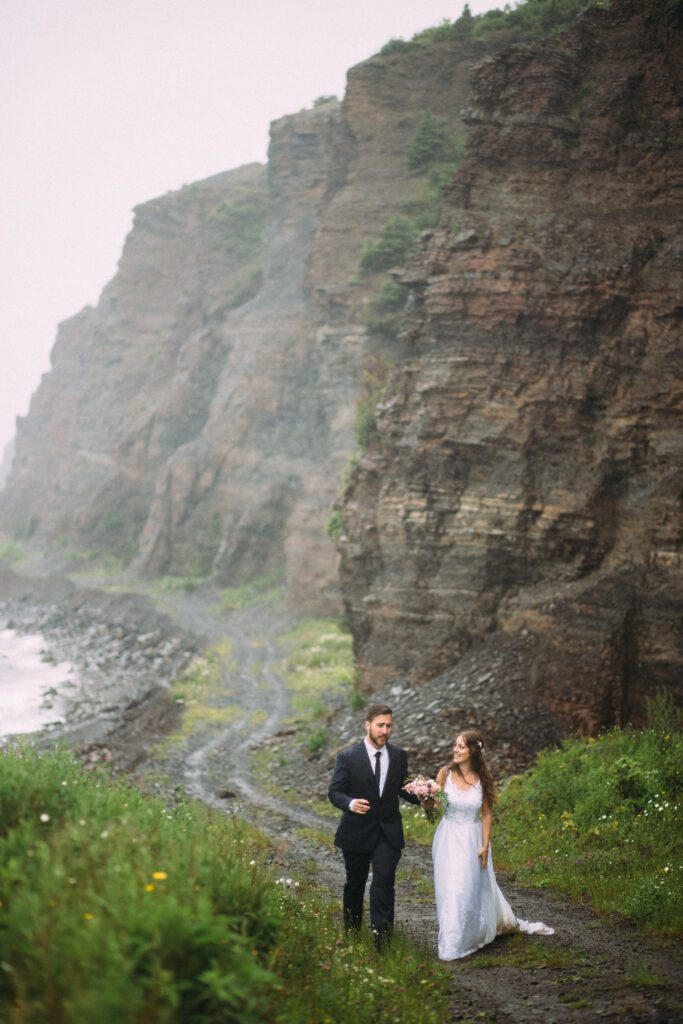 bride and groom explore beneath towering sea cliffs on their elopement day