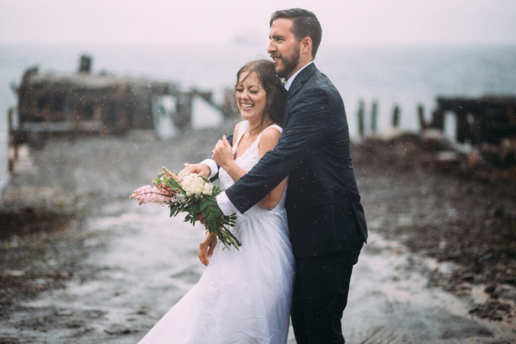 bride and groom laugh in the pouring rain during their elopement day