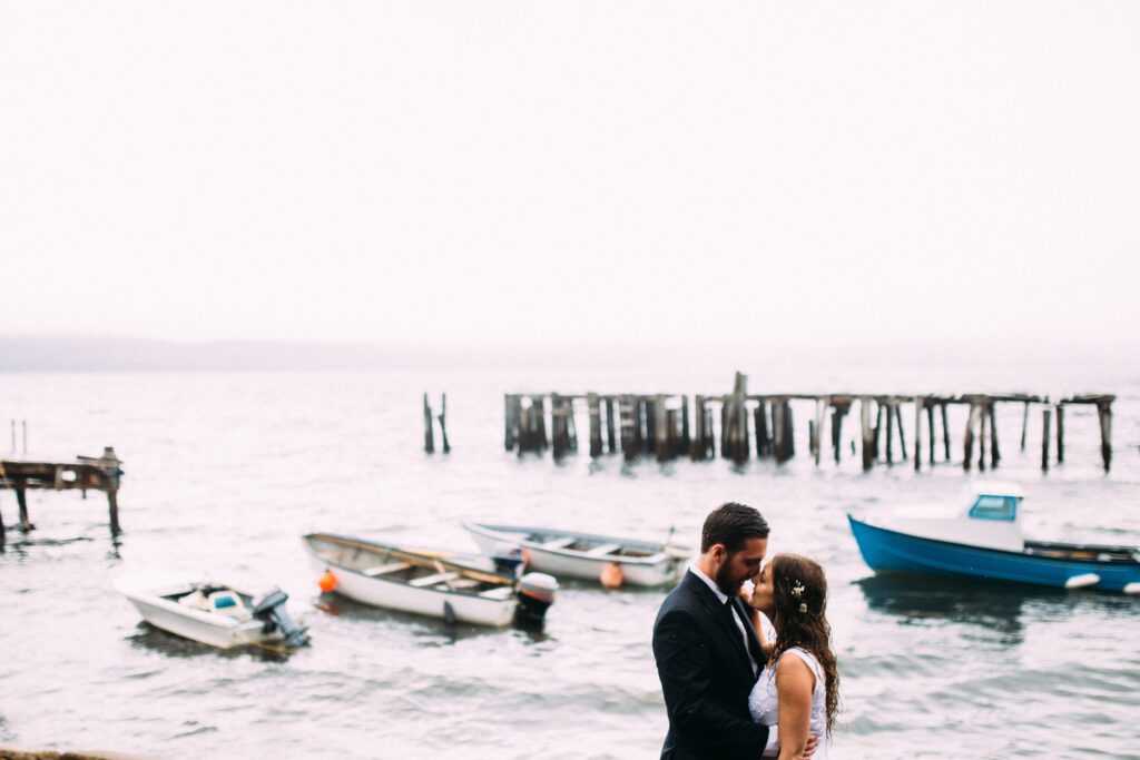 bride and groom hold each other close with boats in the background