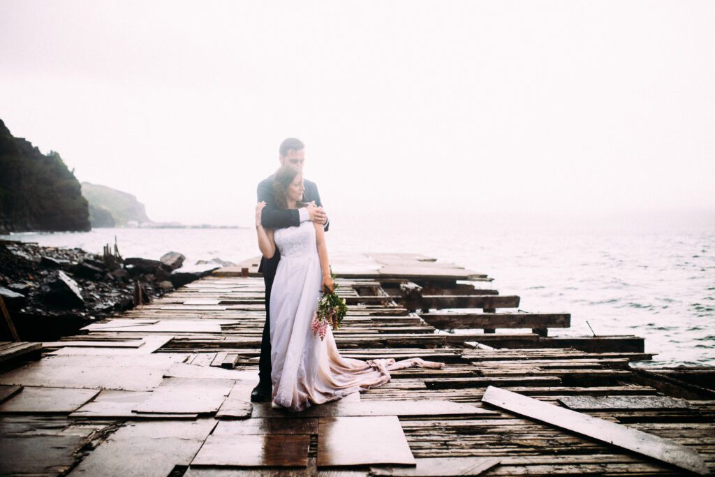 bride and groom hold each other on a pier in the pouring rain on their Newfoundland elopement day