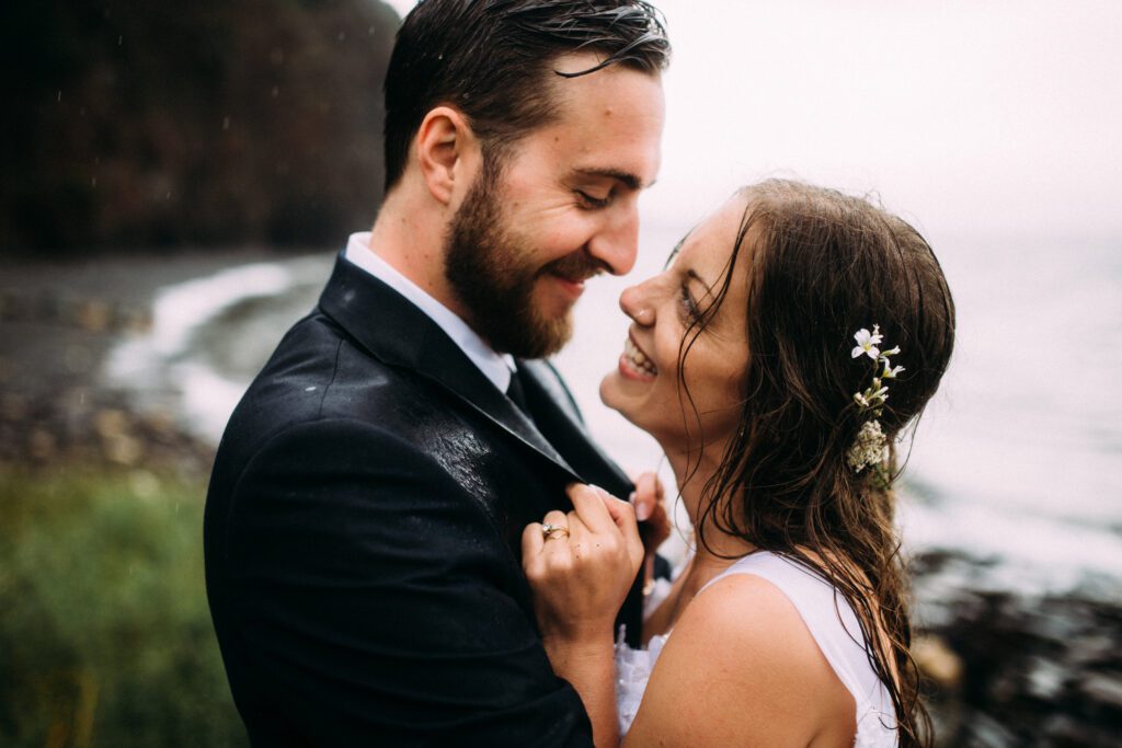 bride and groom grin at each other in the pouring rain during their elopement