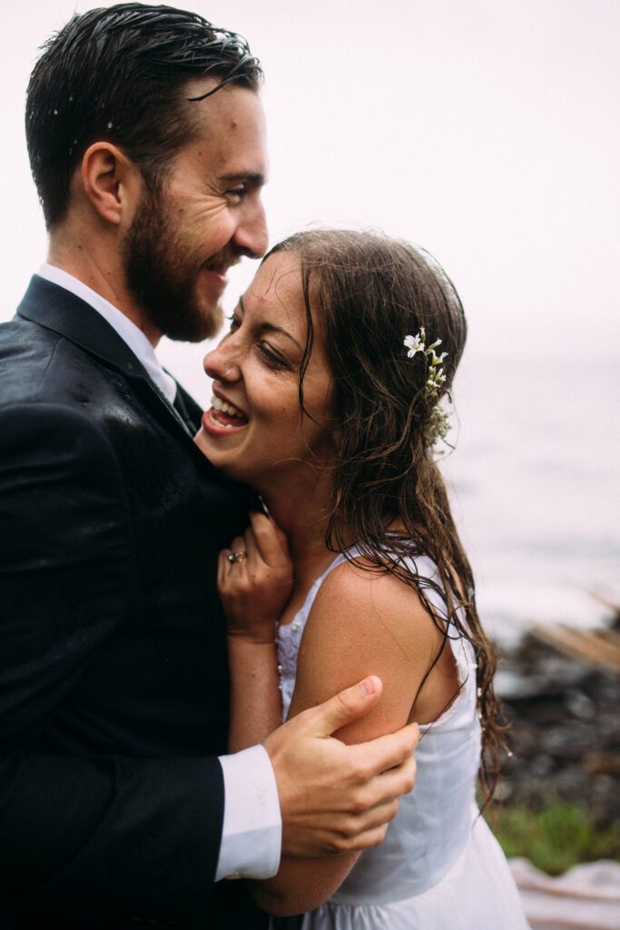 bride and groom laugh and hold each other in the rain