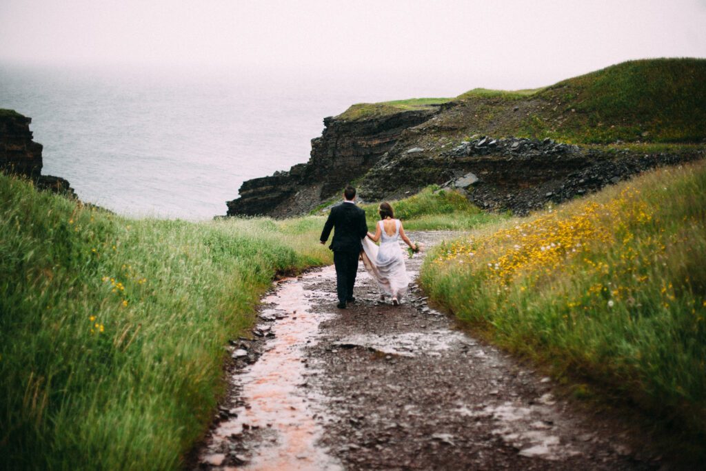 bride and groom walk down path surrounded by green fields during their Newfoundland elopement