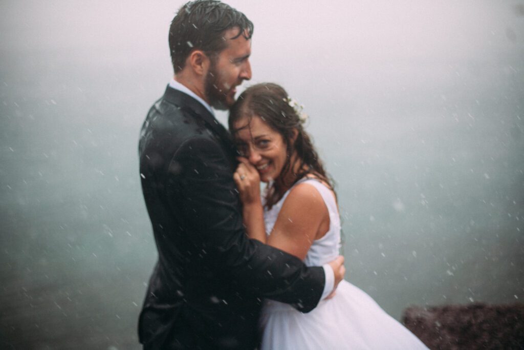 bride and groom laugh in the rain