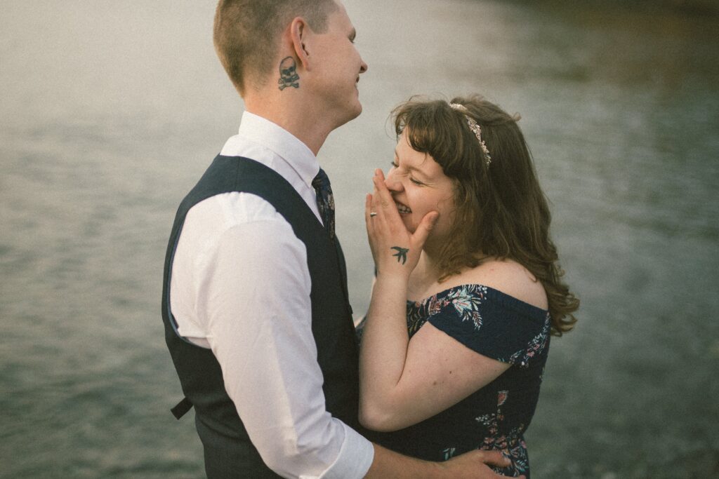 bride and groom laugh by the water's edge on their elopement day
