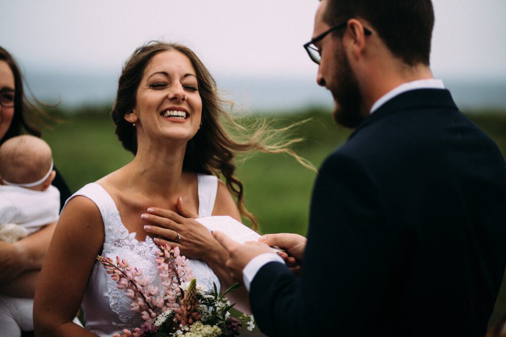 bride laughs and holds a hand over her heart while groom reads vows