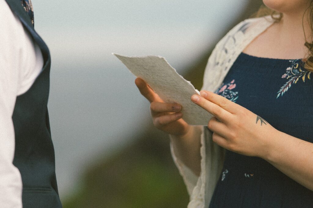 bride reads vows from handmade paper during elopement ceremony near a cliff
