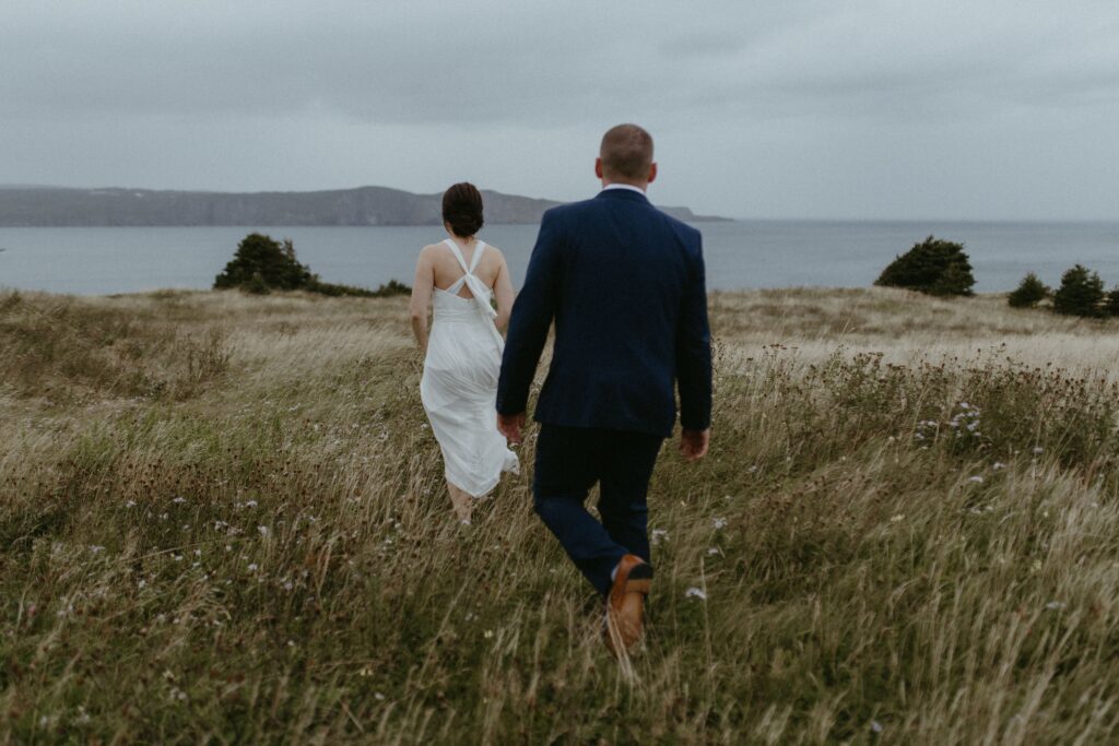 bride and groom explore grassy field above the ocean during Newfoundland elopement