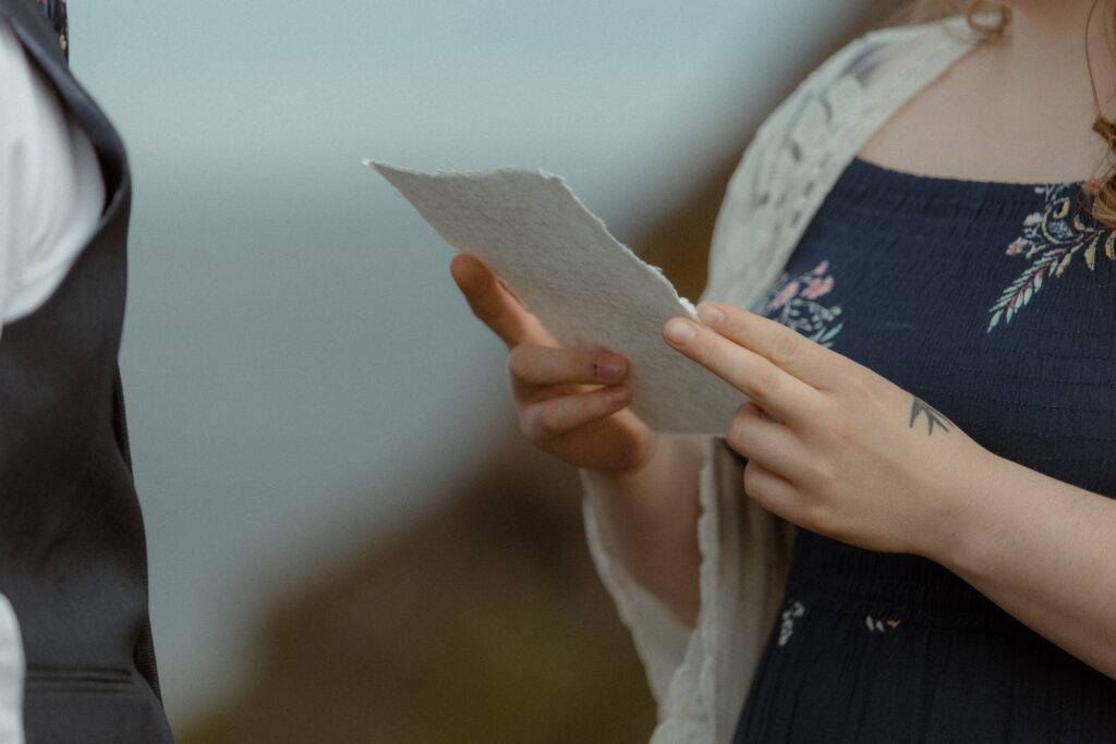 bride reads vows from handmade paper during elopement ceremony near a cliff