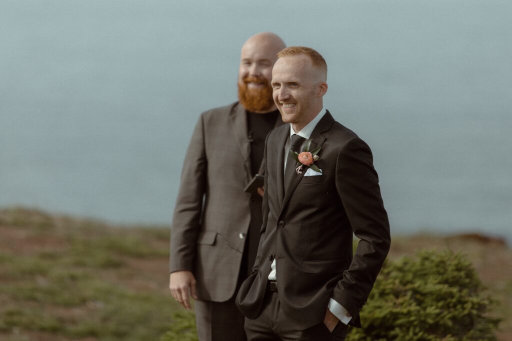 groom grins as he sees his bride for the first time on hiking trail in Newfoundland