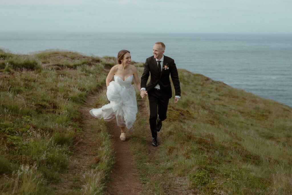 bride and groom laugh and run in oceanside meadow during their Newfoundland elopement