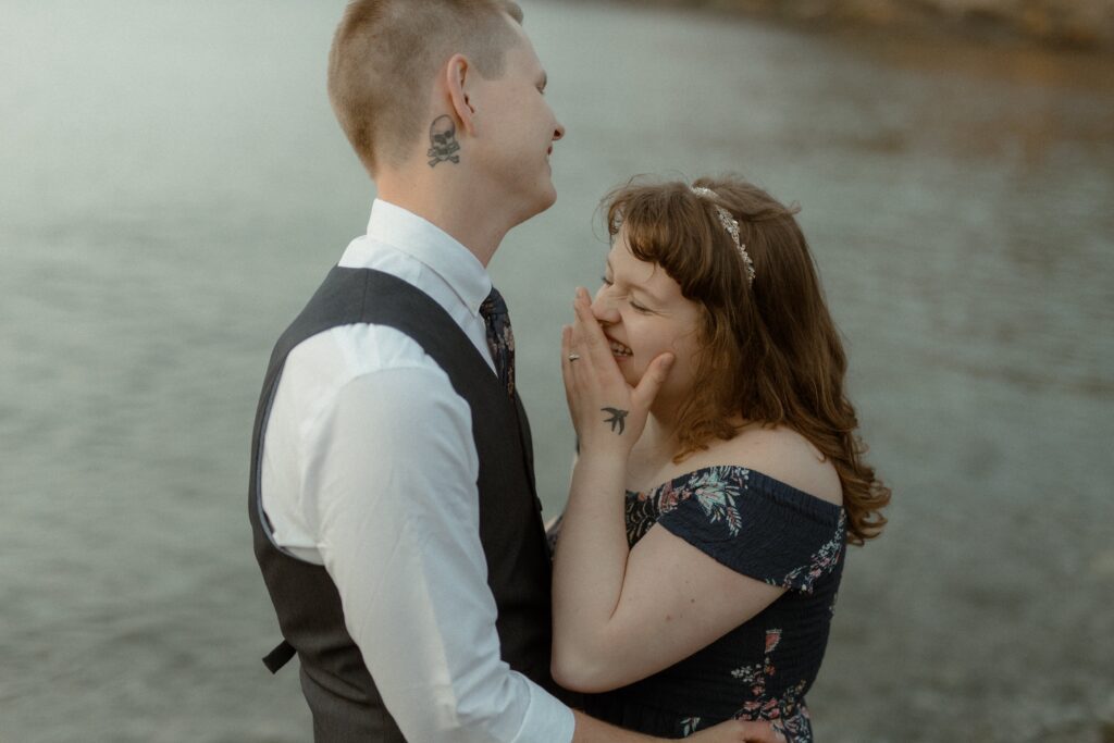 bride and groom laugh by the water's edge on their elopement day