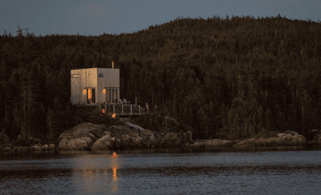 a modern, Scandinavian style cabin on the edge of the ocean surrounded by trees