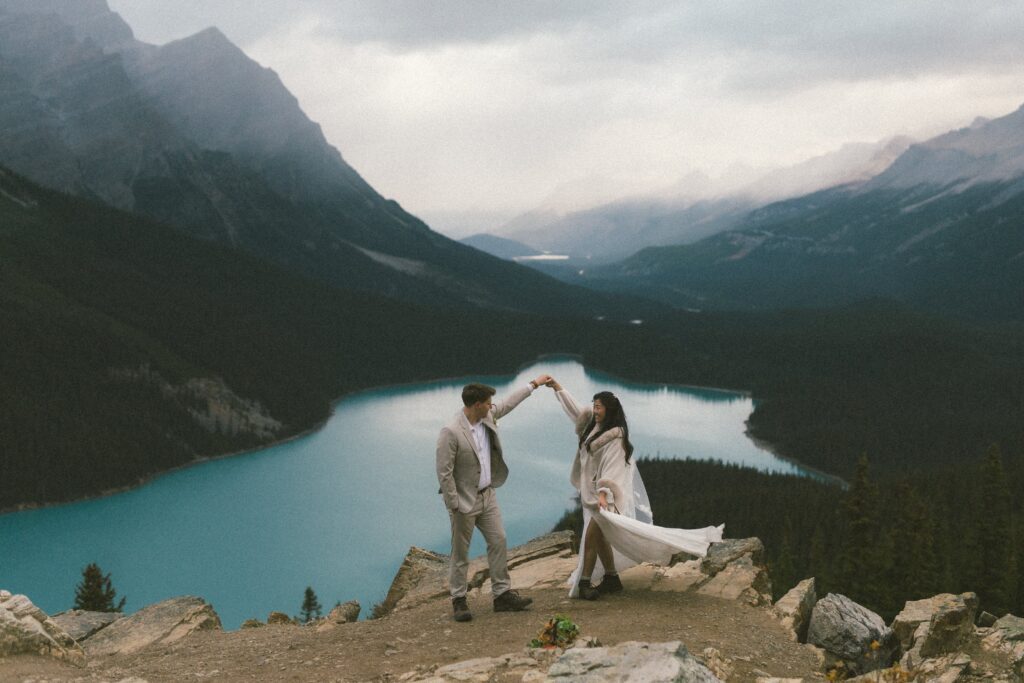 Bride and groom dance on rocky outcrop above turquoise Peyto Lake with mountains behind