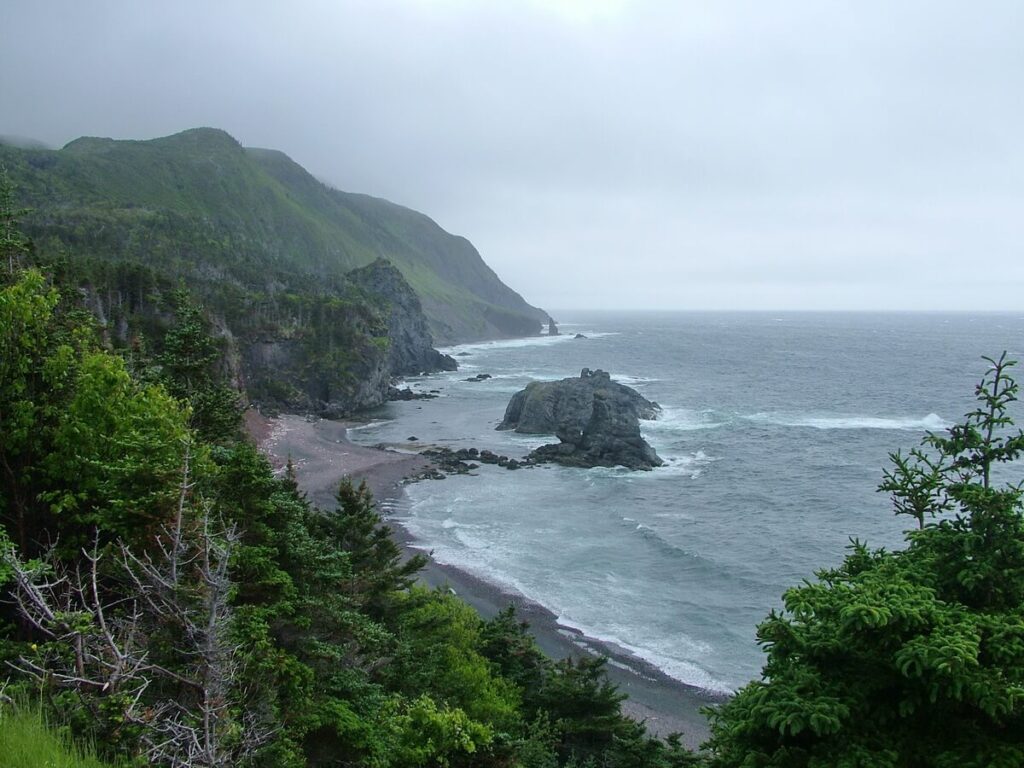 Foggy coastal vista with lush green mountains and beaches at Green Gardens trail in Gros Morne National Park