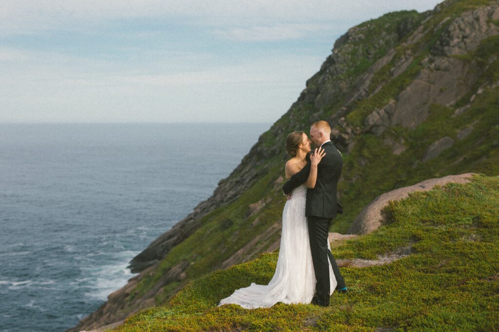 bride and groom hold each other on the edge of a dramatic sea cliff in Newfoundland