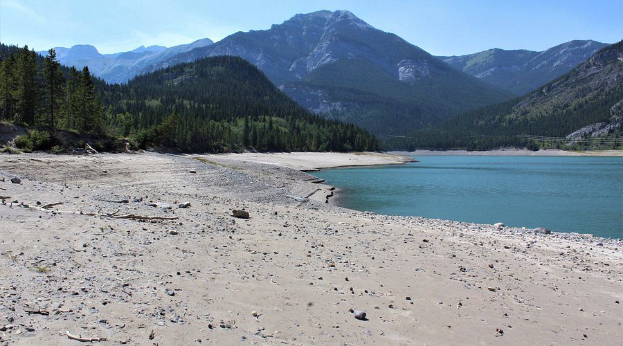 A sandy beach leads to a lake with mountains in the background at Barrier Lake, Kananaskis
