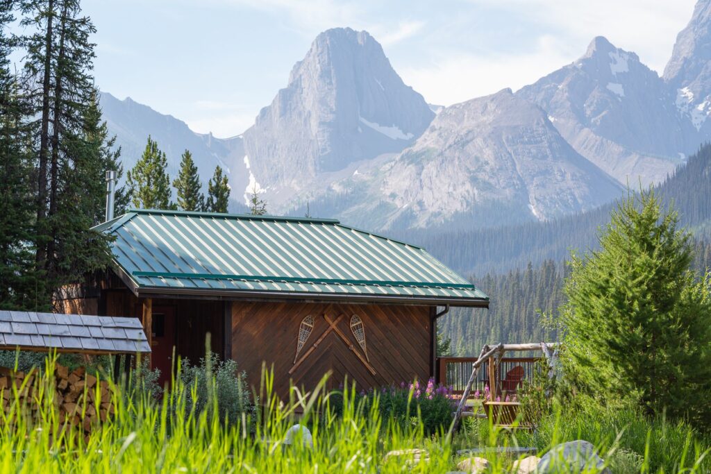 a rustic cabin in a meadow with mountains in the background in Kananaskis, Alberta