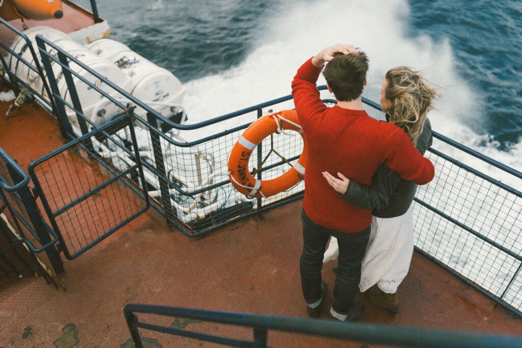 couple stand on the deck of ferry with waves crashing around them