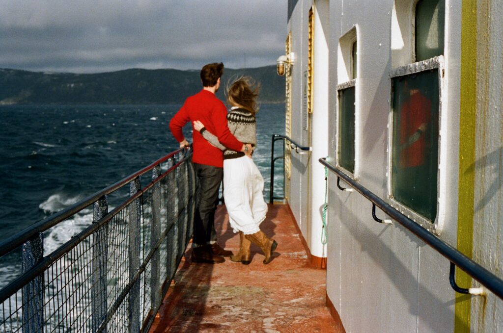 couple in nordic outfits watch the waves on the deck of a ferry