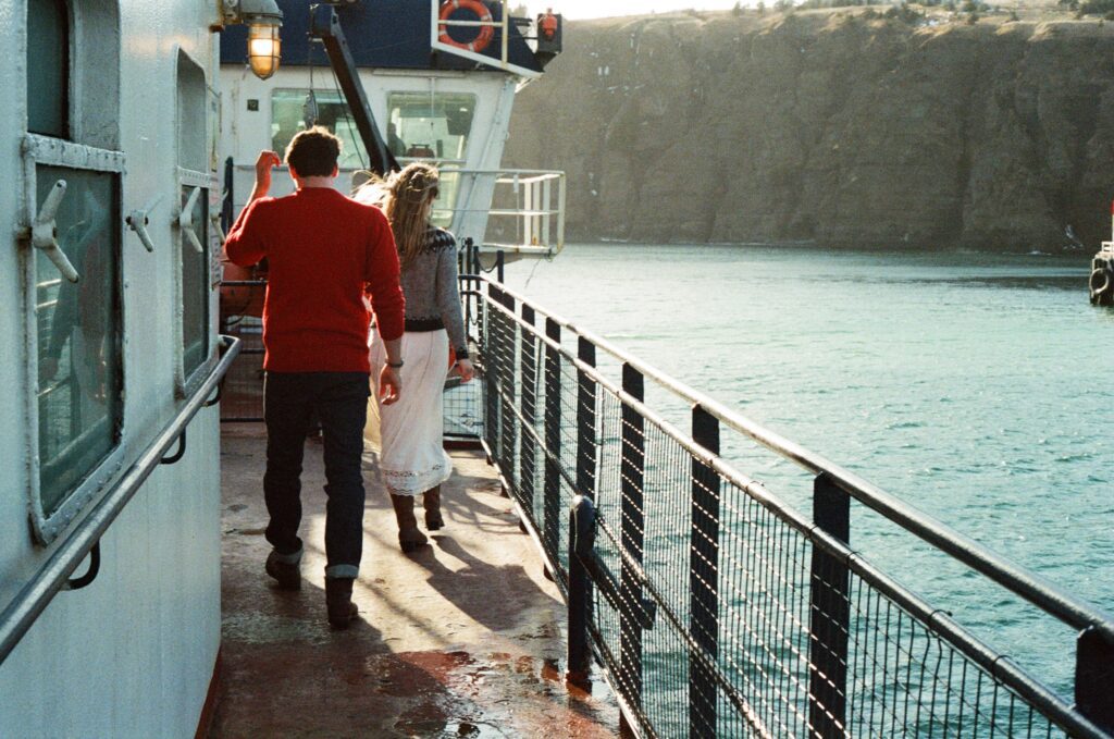 couple walk along the deck of a ferry in the sun