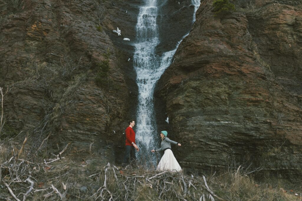 couple run toward each other in front of a towering waterfall