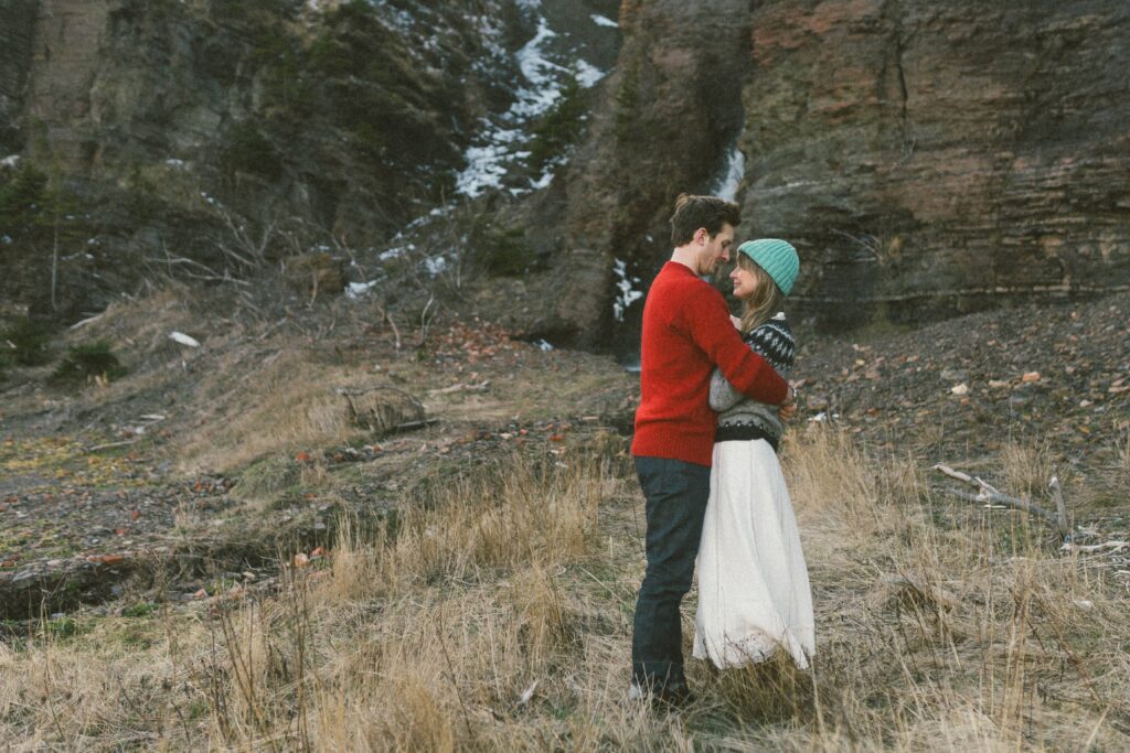 couple in wool sweaters cuddle in tall grass