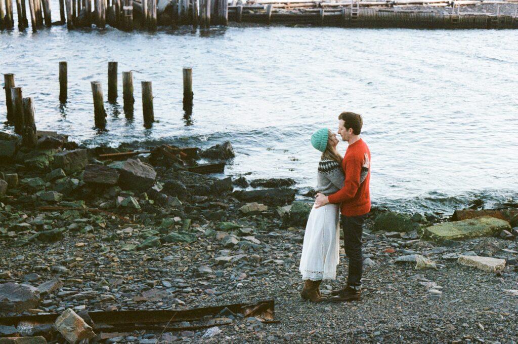 couple in wool sweaters embrace by the ocean