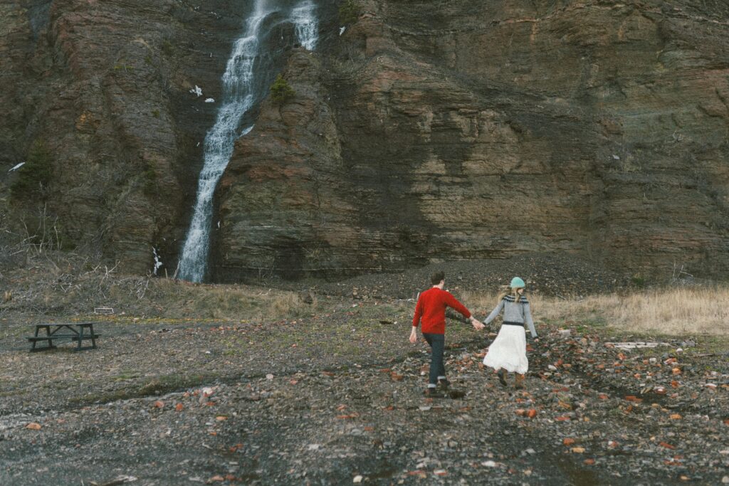 couple in wool sweaters walk toward a waterfall