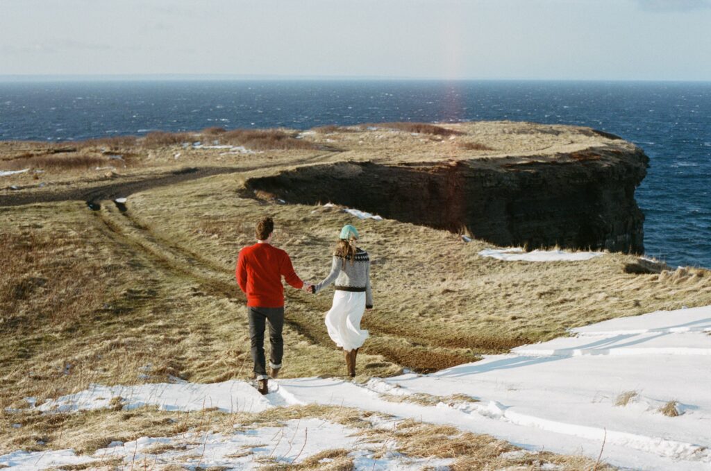 couple in wool sweaters follow a path through the grass to a cliff